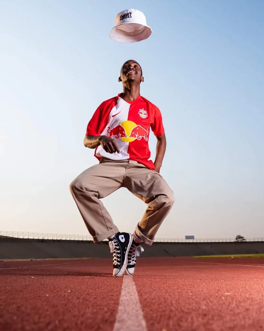 Tebza Diphehlo balanced on his toes on an outdoor running track at dusk, in a Red Bull jersey, a cap spinning above his head.