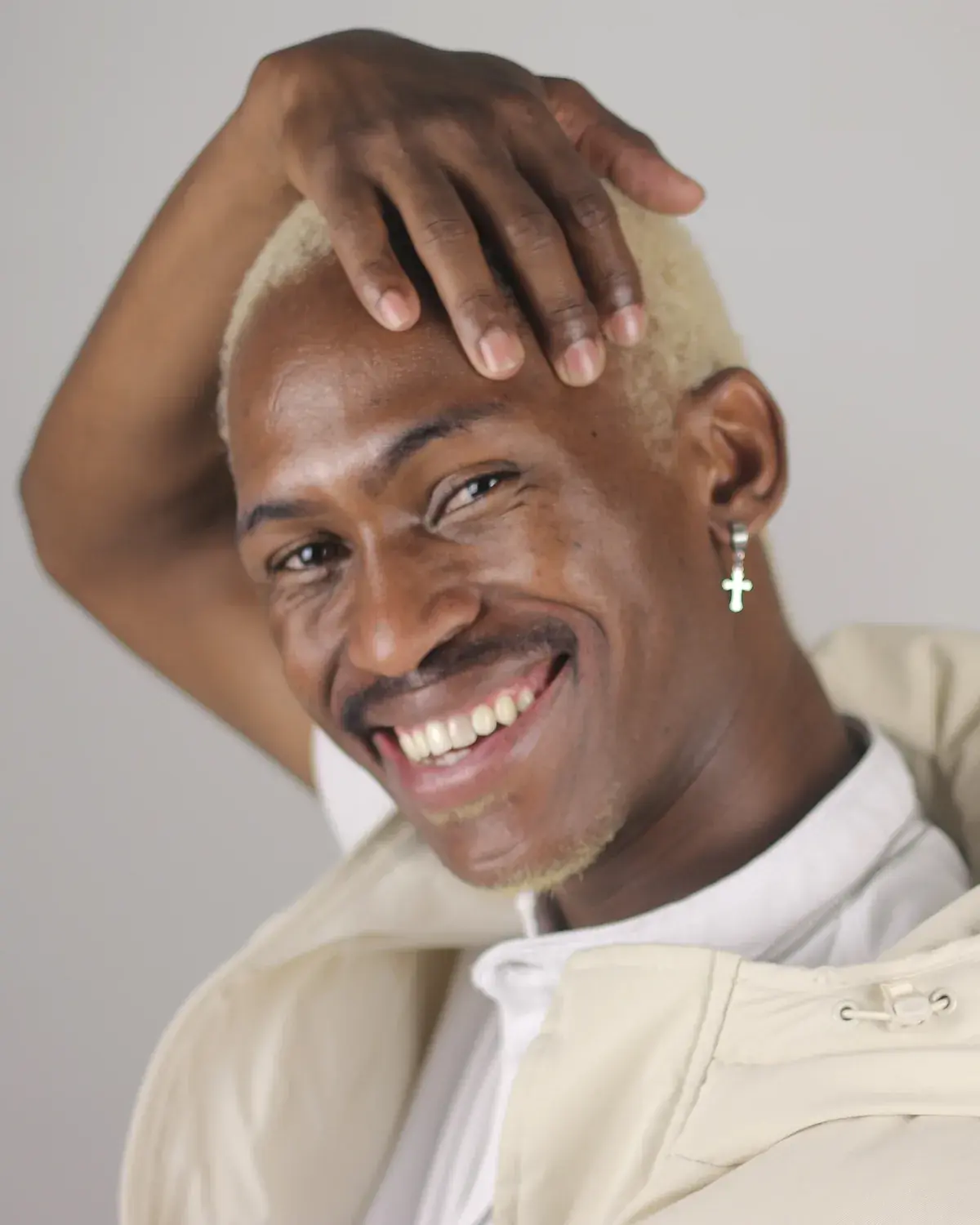 Tebza Diphehlo laughing with one hand on his head, photographed against a plain pale studio wall.
