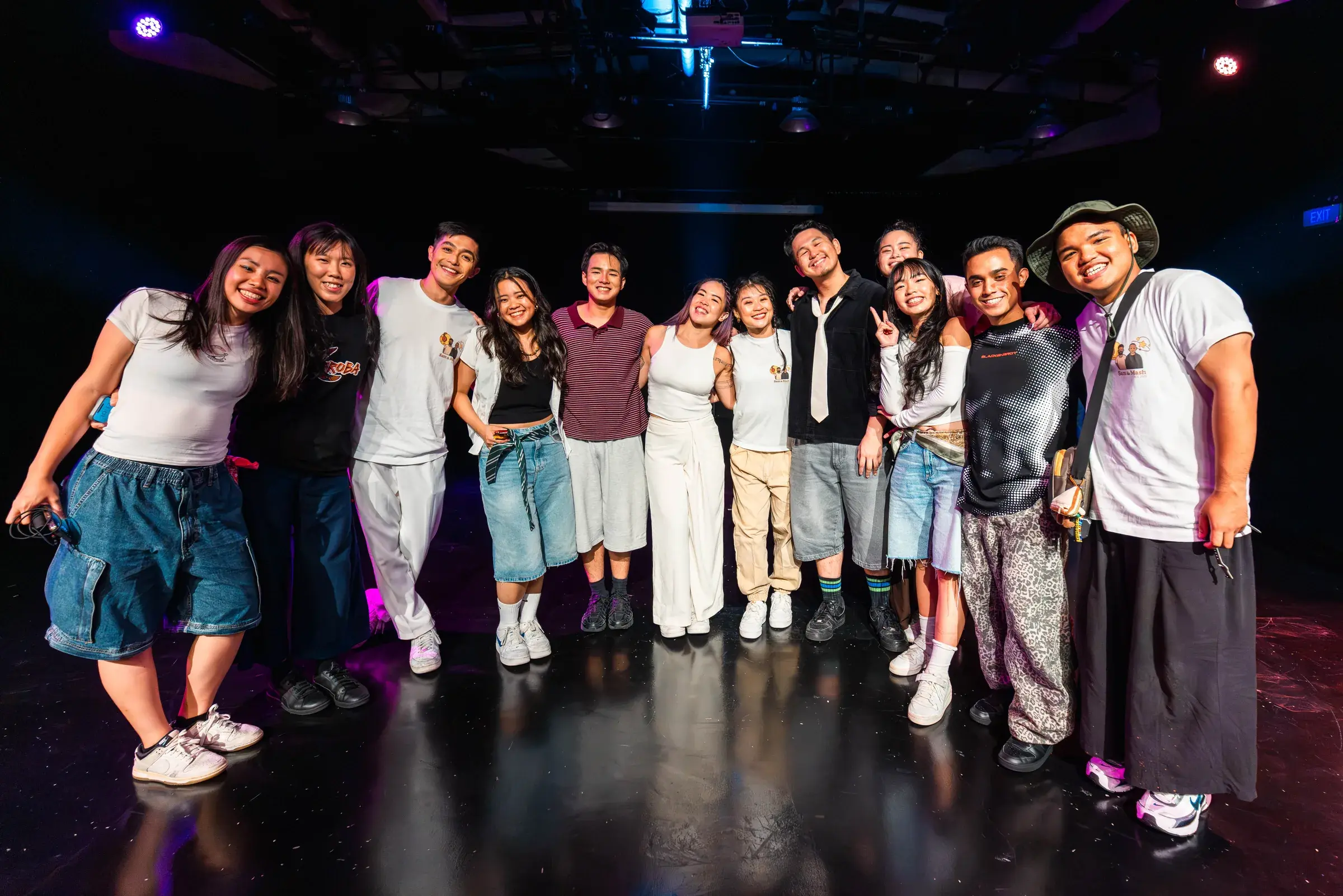 A long line of people with arms around each other, smiling at the camera on stage.