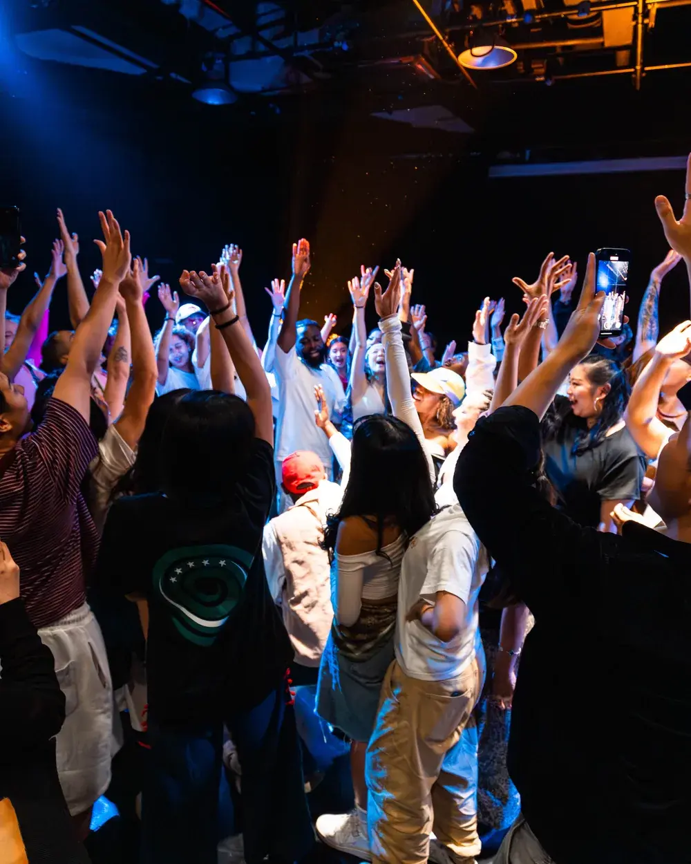 The ACE 2025 showcase audience with their hands in the air under stage lights.