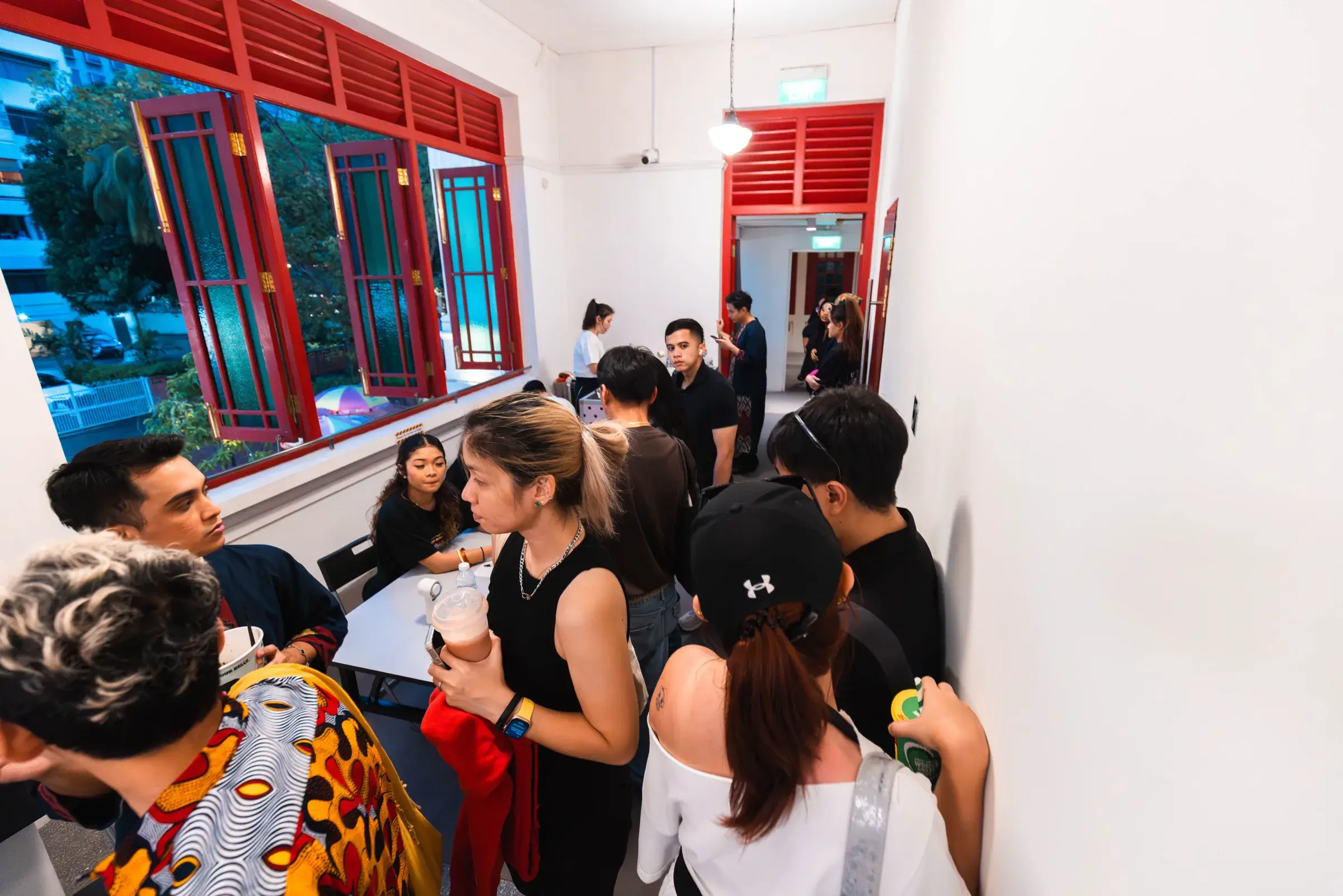 Attendees standing and talking in a red-shuttered shophouse corridor before the ACE 2025 show.