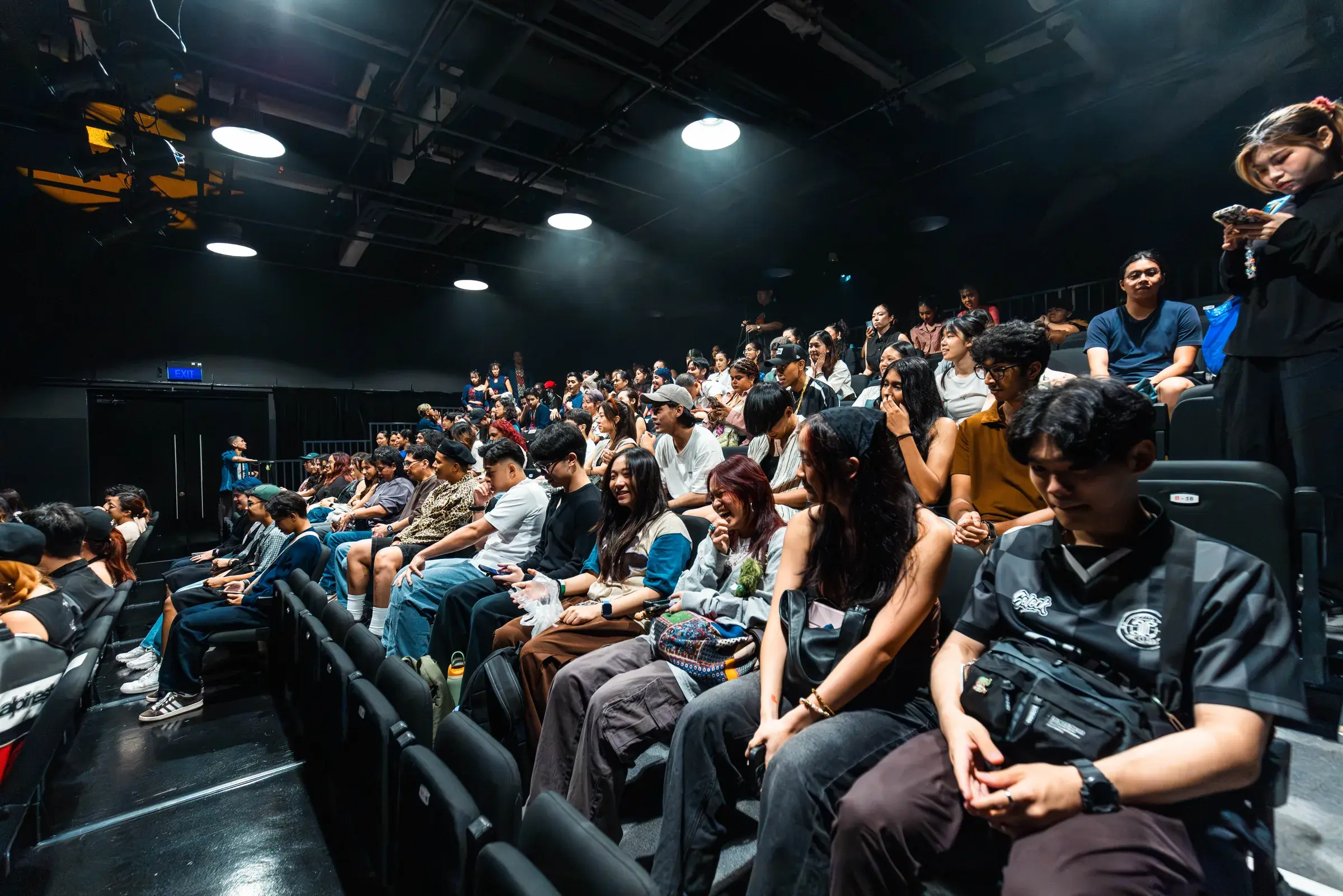 Audience members filling the raked seating of a black box theatre before the show.