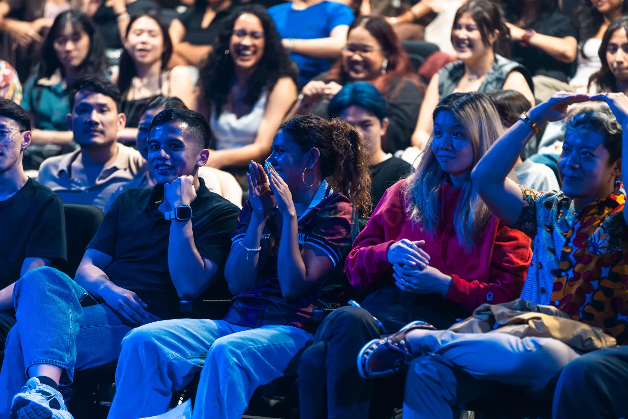 Three audience members in theatre seats, one clapping and two laughing at something on stage.