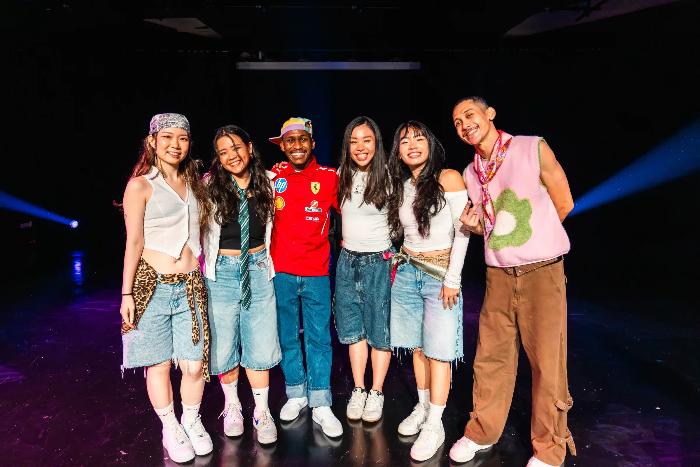 Six people standing arm in arm on a stage, smiling at the camera after the show.
