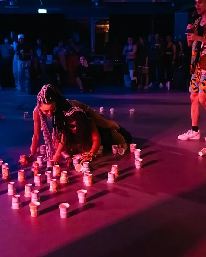 A dancer low to the floor mid-move at the ACE 2025 showcase, lit red and blue among rows of candles.