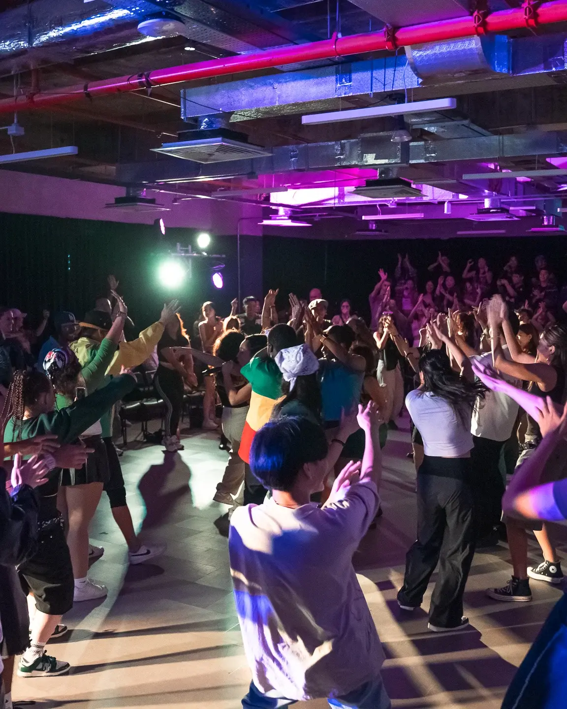 A full studio of dancers at ACE 2025 following a routine together under stage lighting.
