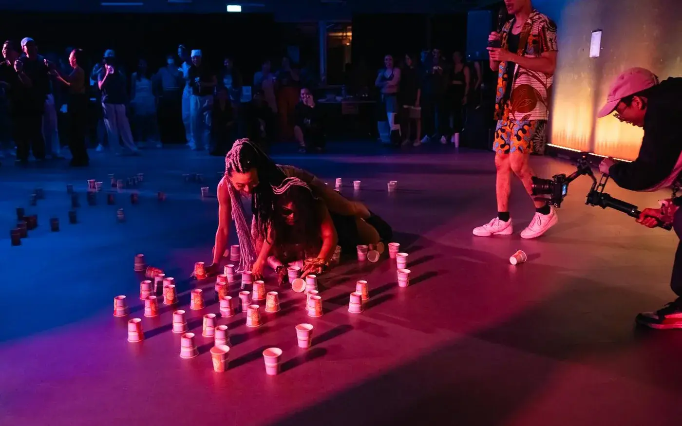 A dancer low to the floor in a pool of light, surrounded by lit candles, performing on stage.