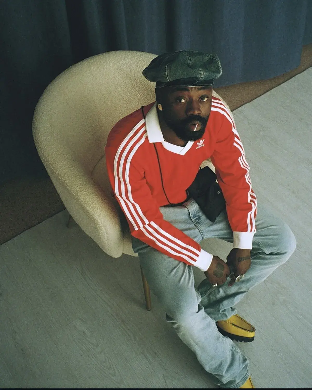 Yemi Osokoya seated in a red Adidas track top and dark cap, looking to camera.